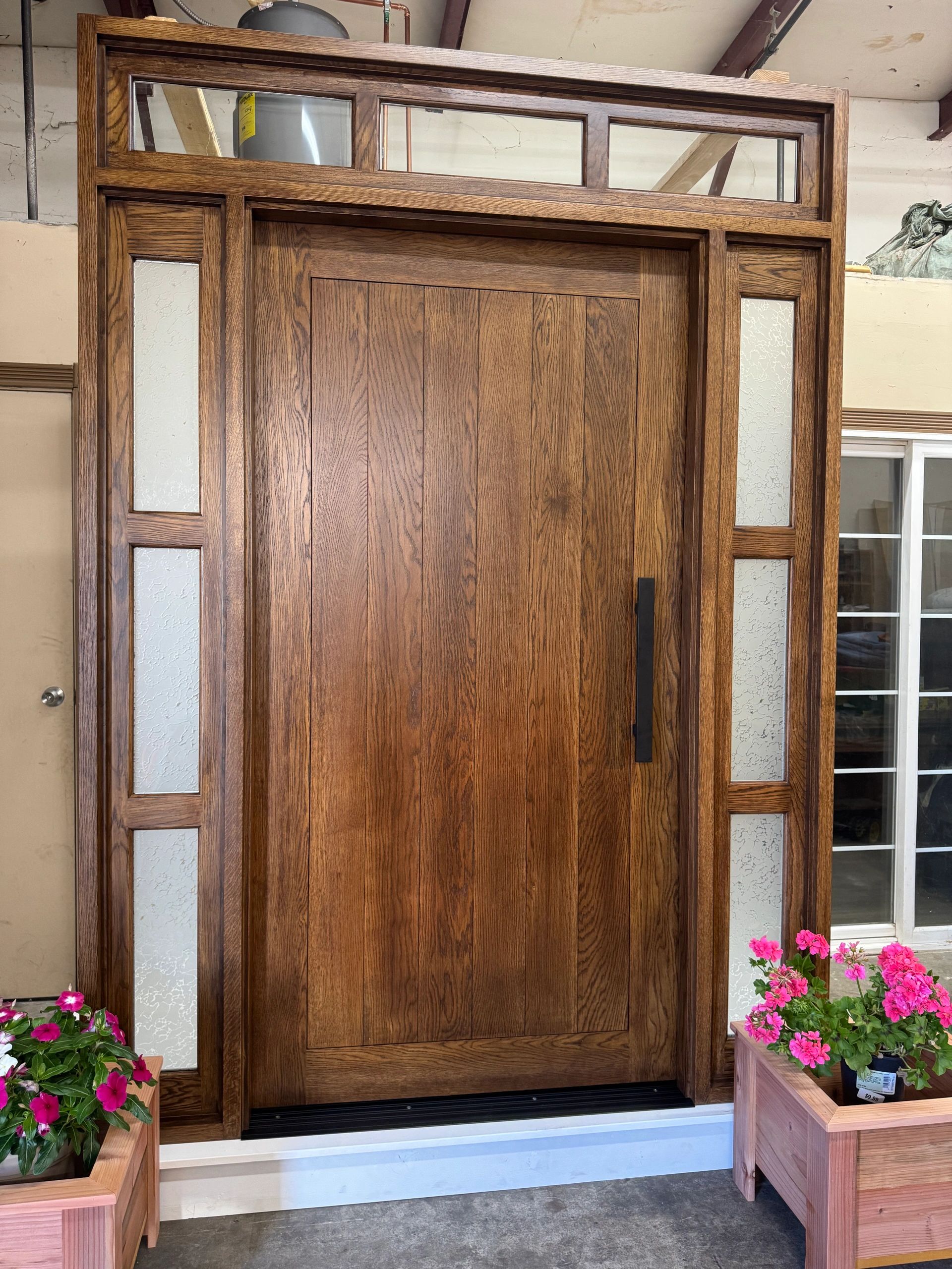 Elegant wooden front door with side glass panels and pink flowers.