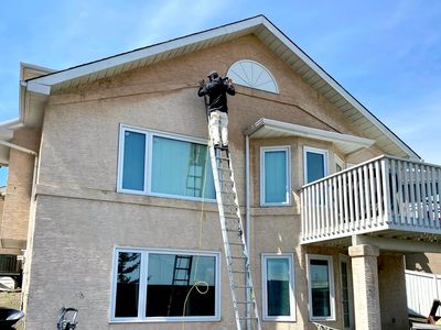 Imagine of a house with a tall lader against it, with a man painting  the peak of the house