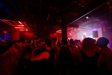 Crowded nightclub with red lighting and a lively crowd.