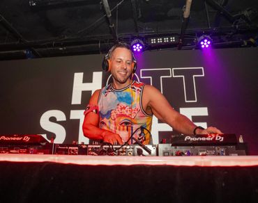 DJ performing energetically on stage with colorful attire and headphones.
