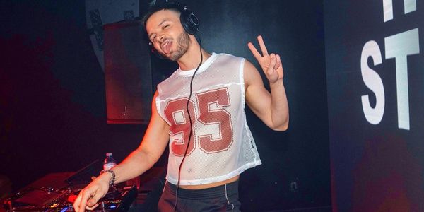 DJ wearing a mesh crop top and headphones, making a peace sign.