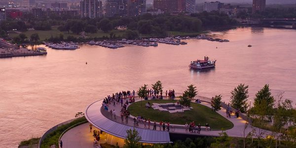 People gather on a waterfront park at sunset with a boat on the water.
