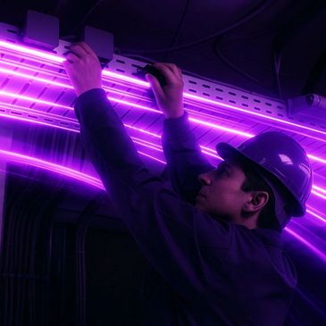 Electrician working with glowing purple cables in a dark environment.