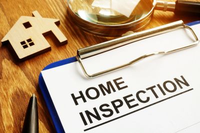 Clipboard with home inspection document, magnifying glass, and wooden house model.