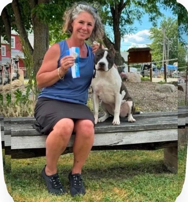 Woman sitting on a bench with her dog and holding a prize ribbon.