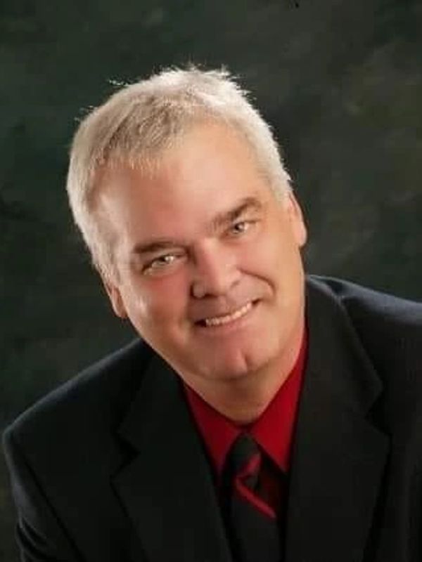 Smiling man in a suit against a dark background.