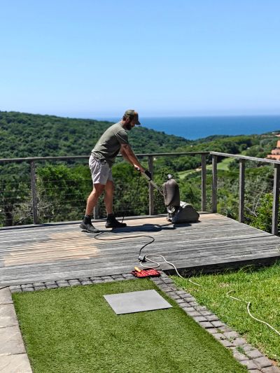 Man sanding a wooden deck with a scenic ocean view.