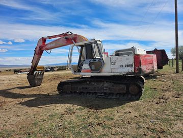 A red and white excavator parked on grassy land under a blue sky.