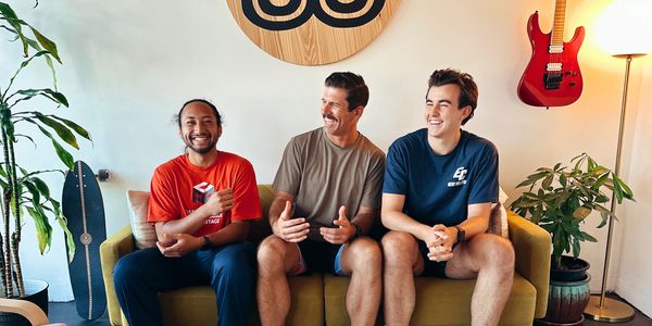 Three men sitting on a couch, smiling and chatting in a cozy room.