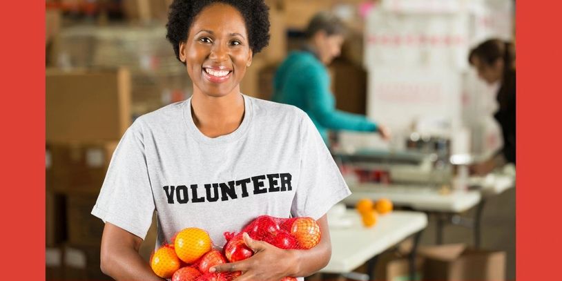 Smiling volunteer holding bags of oranges and apples.