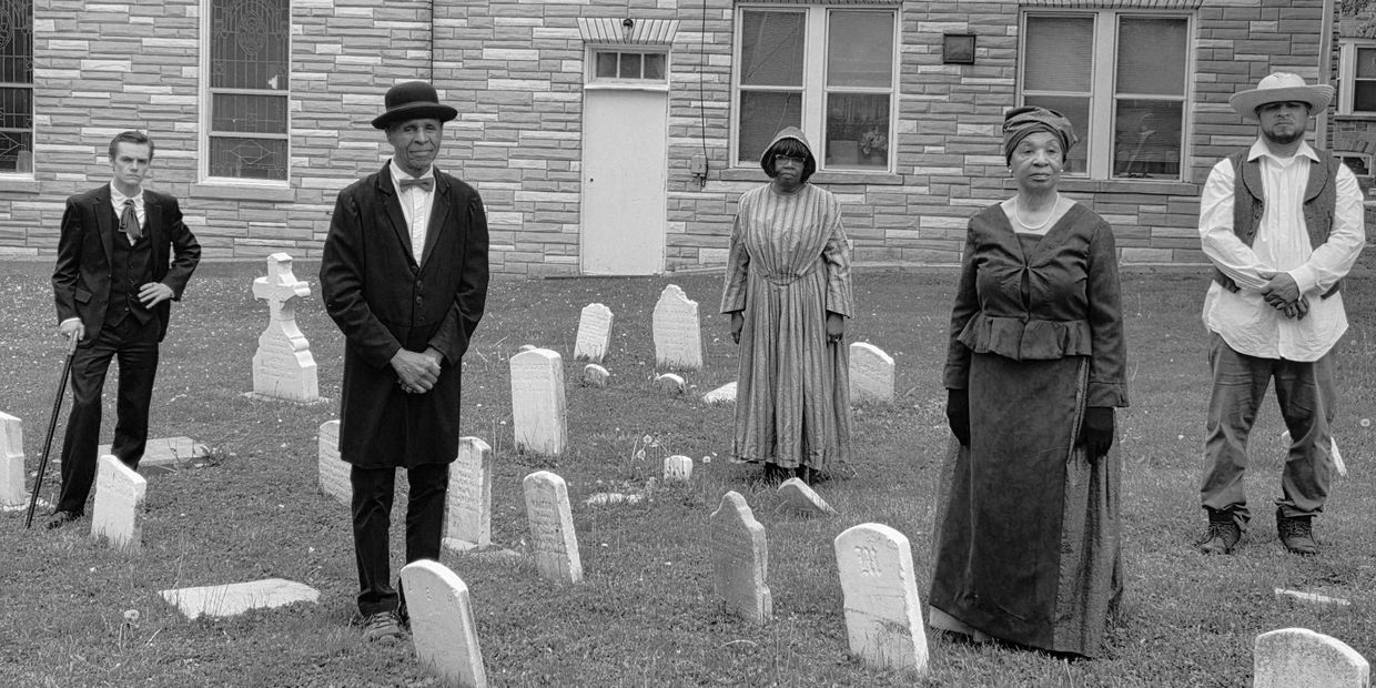 Group of people dressed in historical attire in a cemetery.