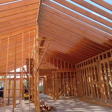 Wooden framework of a house under construction with sunlight casting shadows.