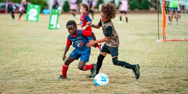 Two kids competing for a soccer ball during a match on a grassy field.