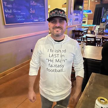A man in a white shirt and black cap smiling in a casual dining setting.
