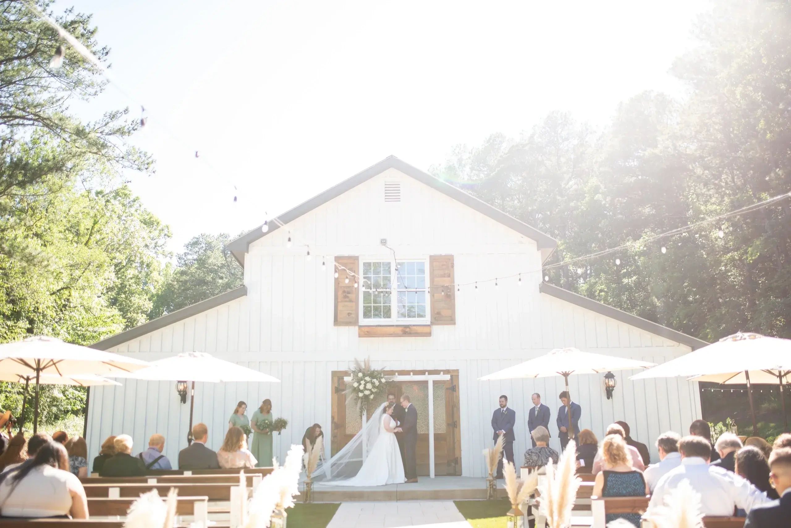 Bride and groom getting married in front of white barn with umbrellas