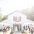 Bride and groom getting married in front of white barn with umbrellas