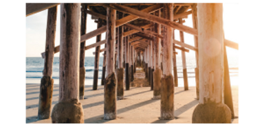 View under a wooden pier with sunlight and ocean waves.
