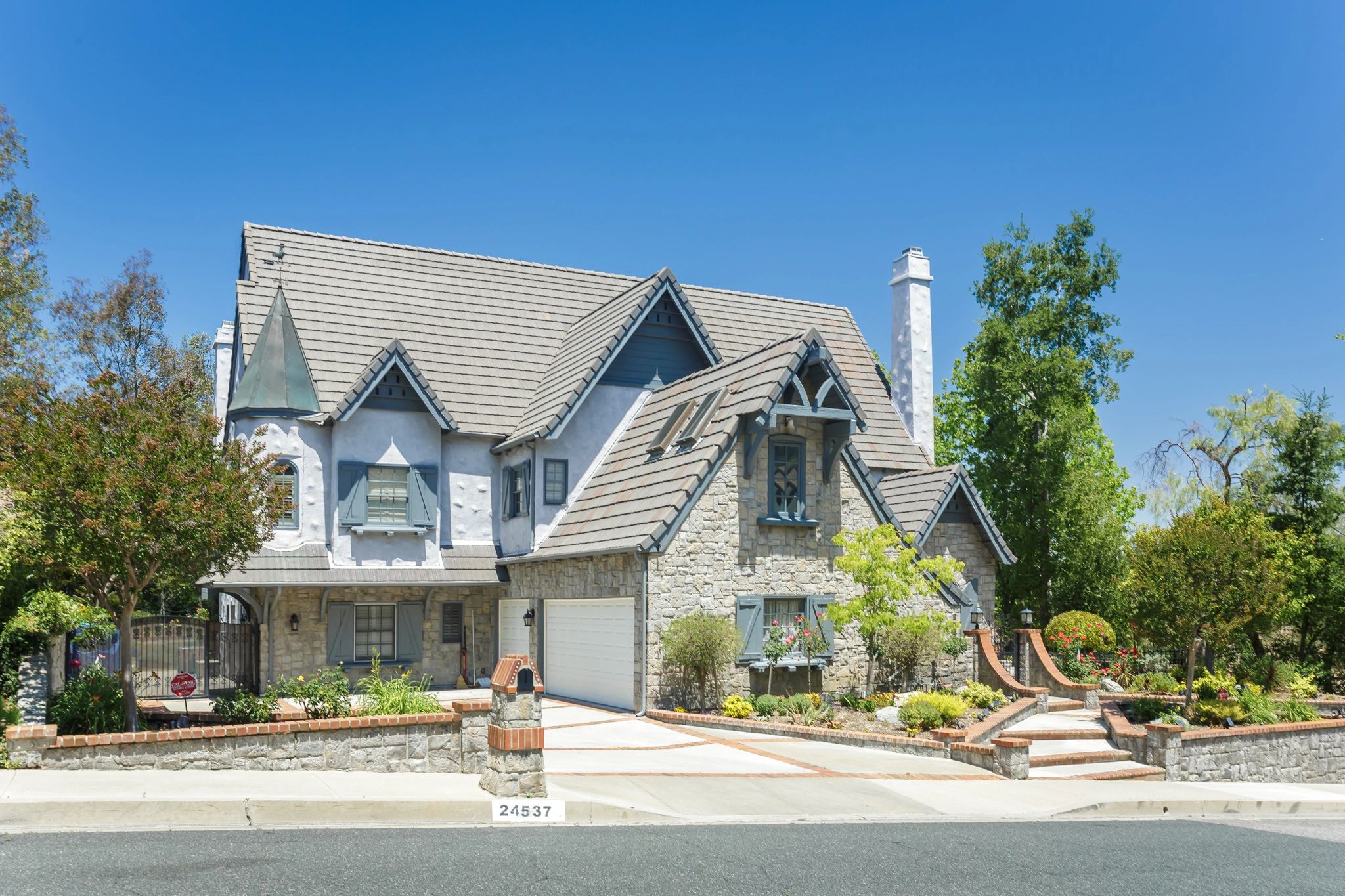 Beautiful stone house with blue shutters and a well-manicured garden under a clear blue sky.