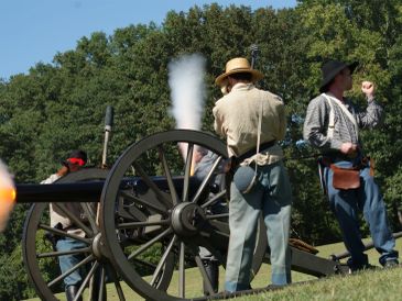 Historical reenactors firing a cannon outdoors.