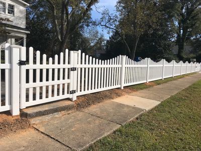 A long white picket fence with a gate along a sidewalk