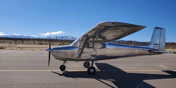 A shiny silver small airplane parked on a runway under clear blue sky.
