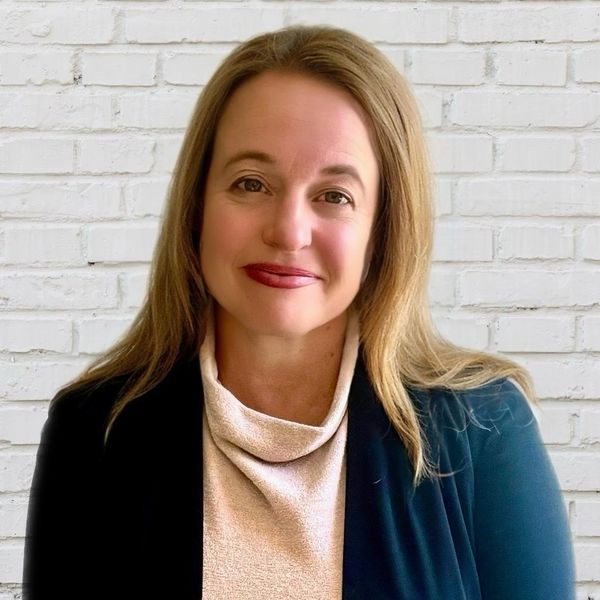 Smiling woman with long hair in front of a white brick wall.