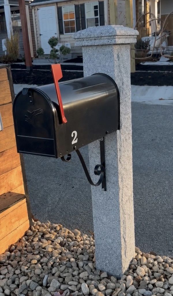 Black mailbox with the number 2 on a stone stand.