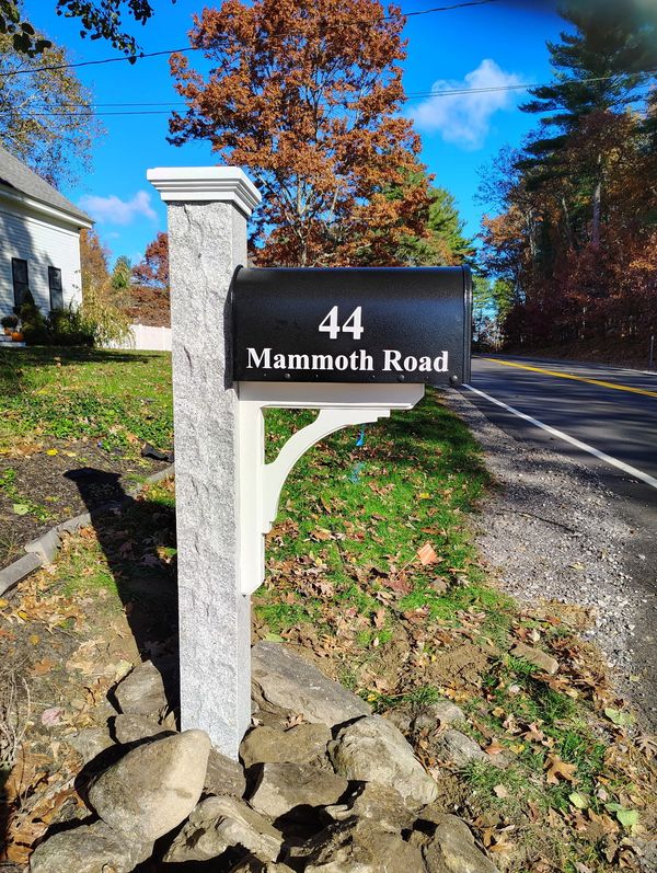 Black mailbox with white text on Mammoth Road next to a rural road.