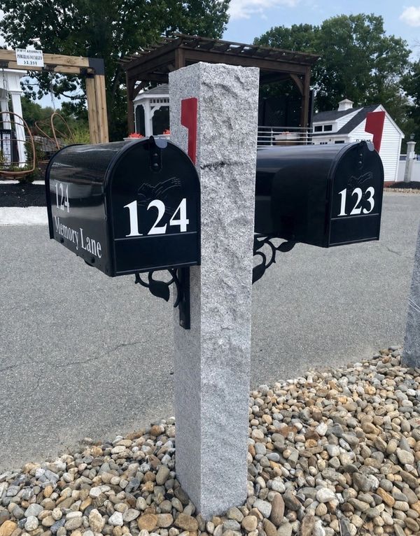 Two black mailboxes on a stone post with pebbles around.