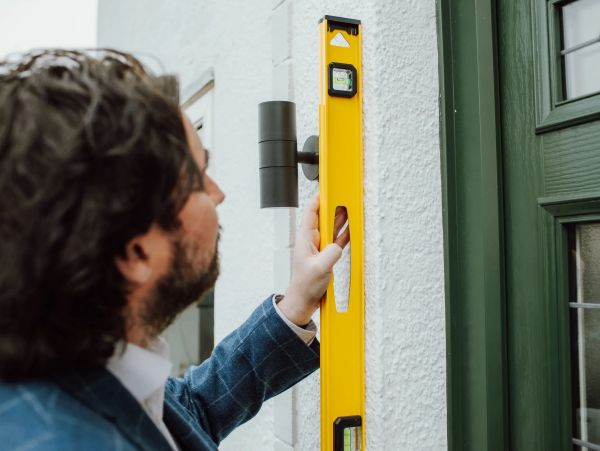 Man using a yellow spirit level on a wall near a door.