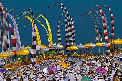 Colorful Balinese ceremonial flags and umbrellas at a large outdoor gathering.