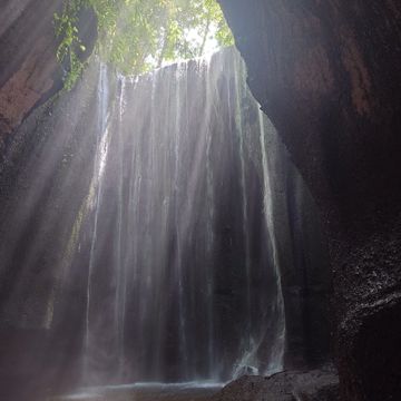 Sunlit waterfall cascading into a serene cave pool.
