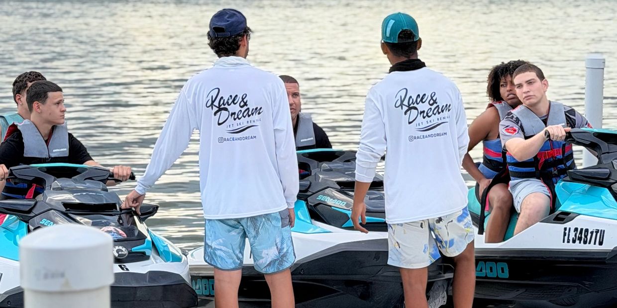People preparing for jet ski rides by the water, wearing life jackets and branded shirts.