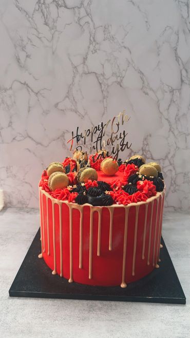 Red and gold drip cake with macarons and black and red frosting.