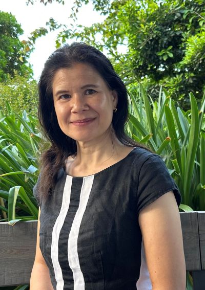 Woman smiling outdoors with greenery in the background.