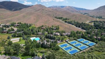 Aerial view of a small community with tennis courts and hills.