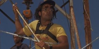 Man wearing a yellow t-shirt and glasses holding a rope on a boat.
