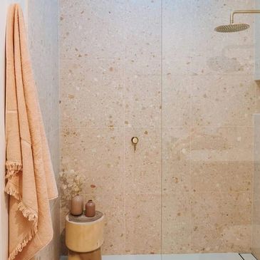 Minimalist shower area with beige tiles and soft peach towel.