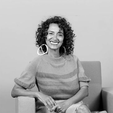 Smiling woman with curly hair sitting on a chair in a cozy sweater.