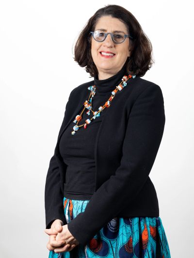 A woman in glasses poses confidently wearing a black jacket and colorful skirt.