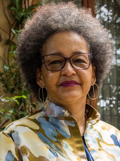 Confident woman with curly gray hair and glasses wearing a patterned blouse.