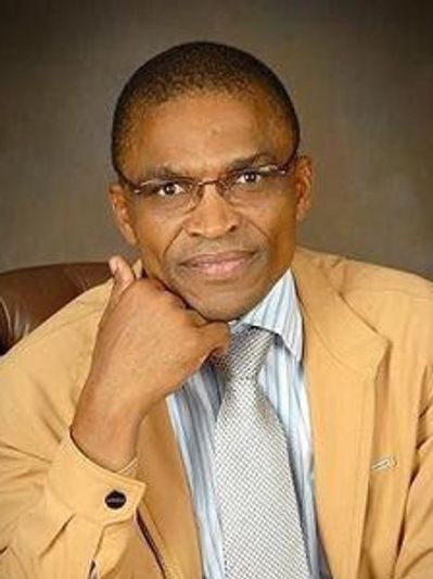 Man wearing glasses, a tan jacket, and tie, posing thoughtfully.