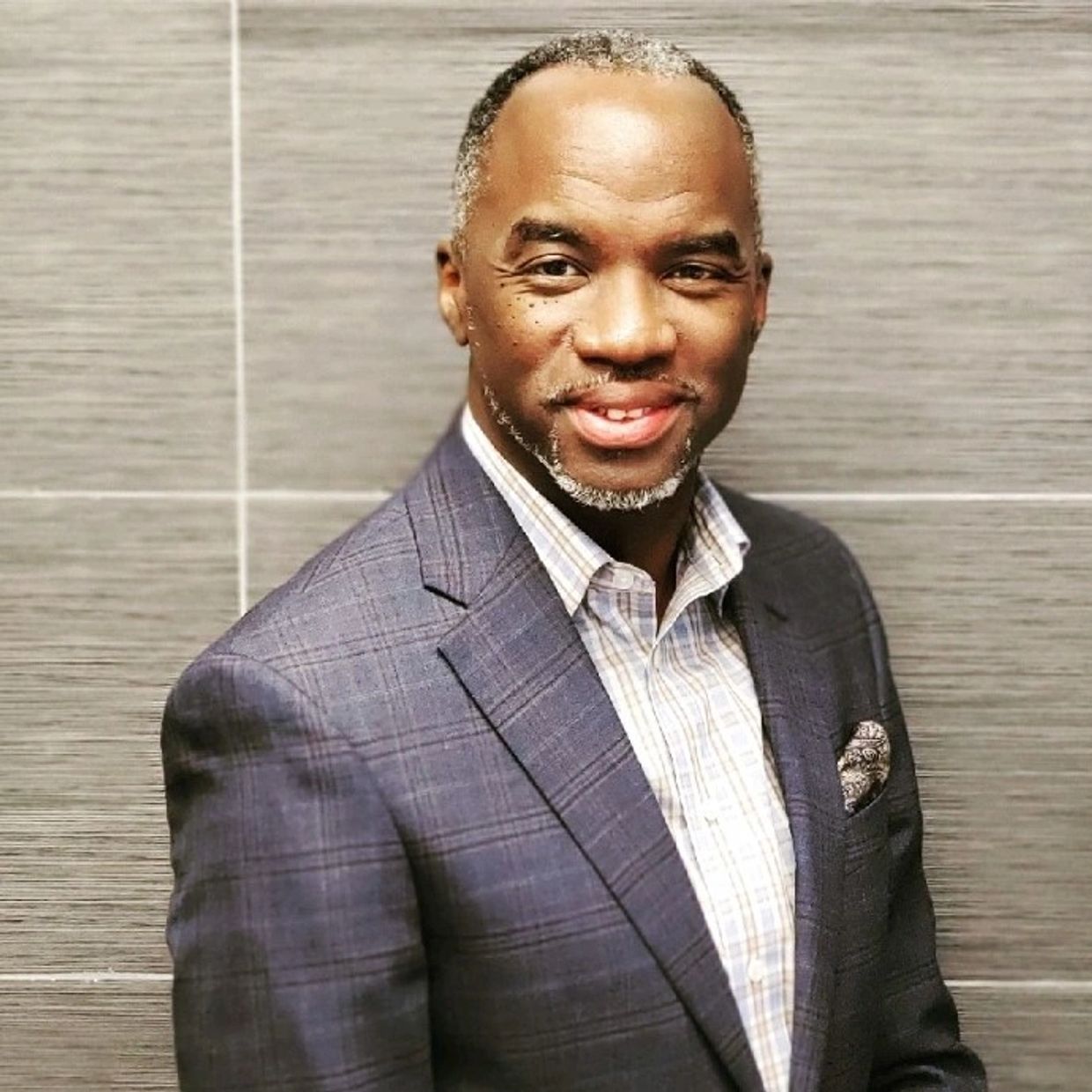 Smiling man in a plaid blazer and checkered shirt.