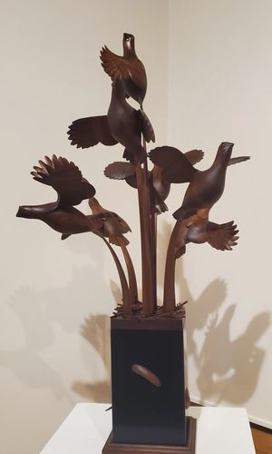 wood sculpture of five birds flying up from the ground with wings spread after being startled.
