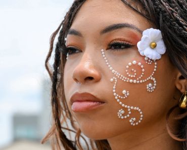 Close-up of a woman with pearl face art and a white flower.