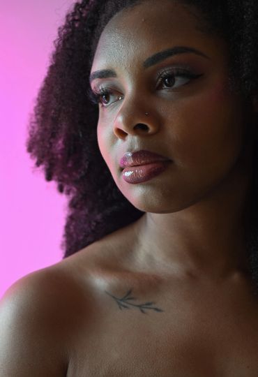 Portrait of a woman with curly hair and a tattoo on her shoulder.