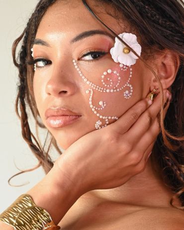 Woman with pearl face art and flower accessory.