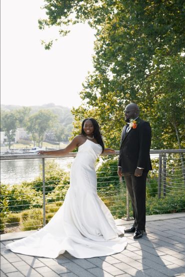 Bride in white gown and groom in black suit outdoors.