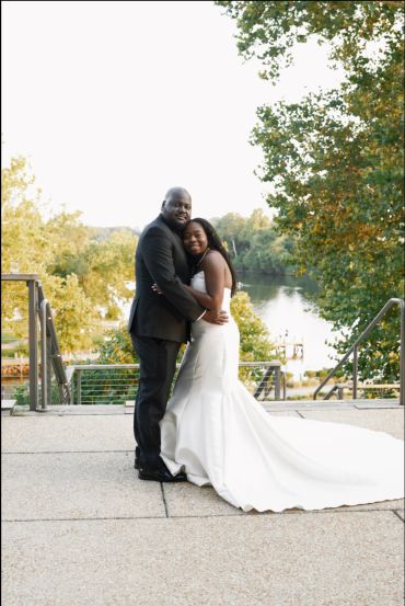 Bride and groom embrace outdoors by a lake.