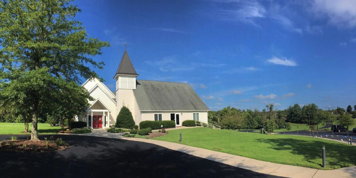 A small white church with a cross on top under a blue sky.